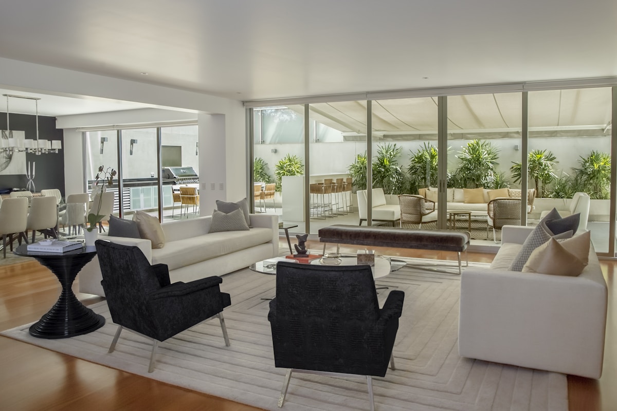 A residence living room opening through full-height glass doors onto a shaded resort terrace with hotel-style lounge seating