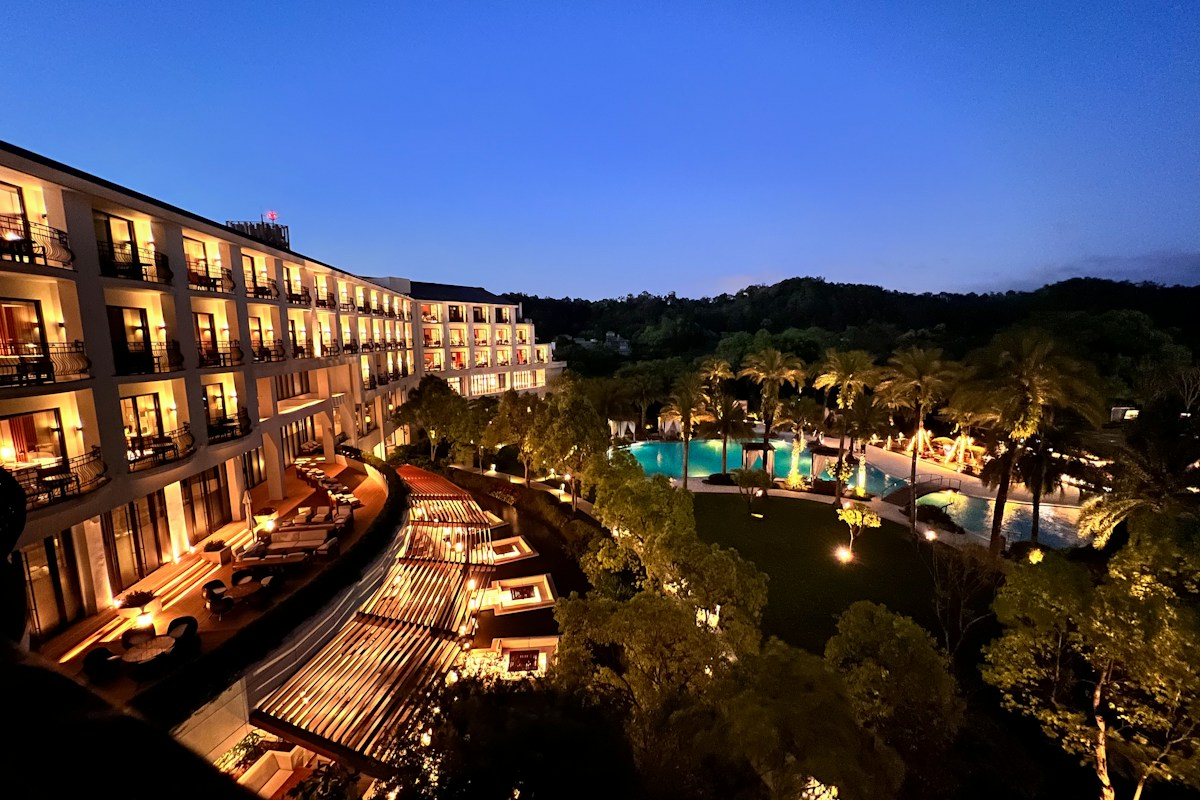 A luxury resort hotel at blue hour with its lit facade, terrace lounge, and illuminated pool surrounded by palm trees
