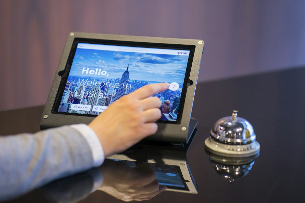 A guest reaching toward a tablet screen, the guest-facing moment where an AI answer has to be right