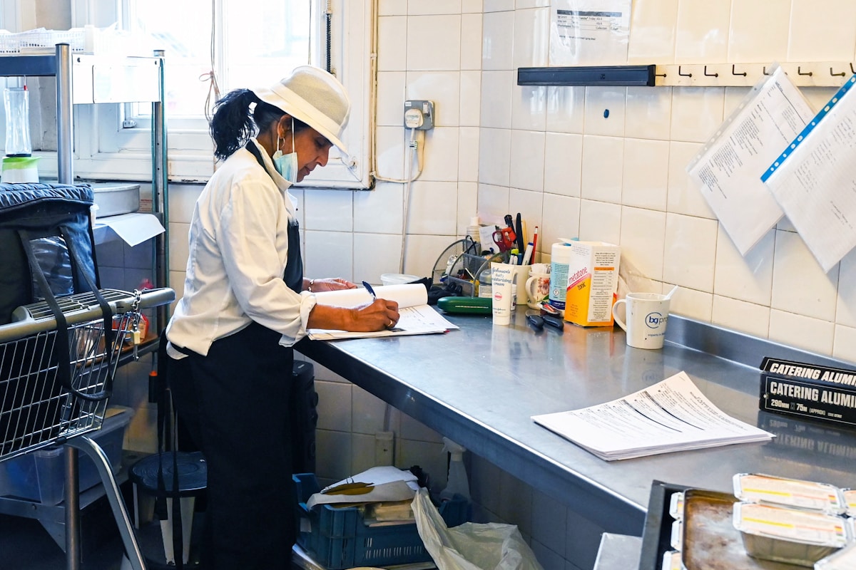 A hospitality team member working through supplier paperwork and delivery notes on a stainless steel counter in a hotel back-of-house kitchen
