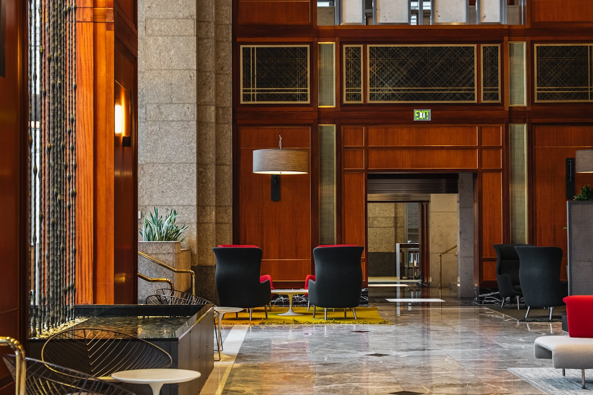 Warm wood-paneled full-service hotel lobby with marble flooring, upholstered lounge seating and elevator vestibule — the long-lived public-space and building-system assets that compete for capital on every hotel renovation list