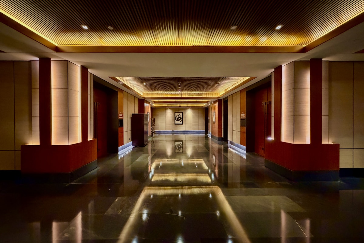 A warm, softly lit luxury hotel corridor lined with guest room doors, each one an electronic lock generating access data the operation can use