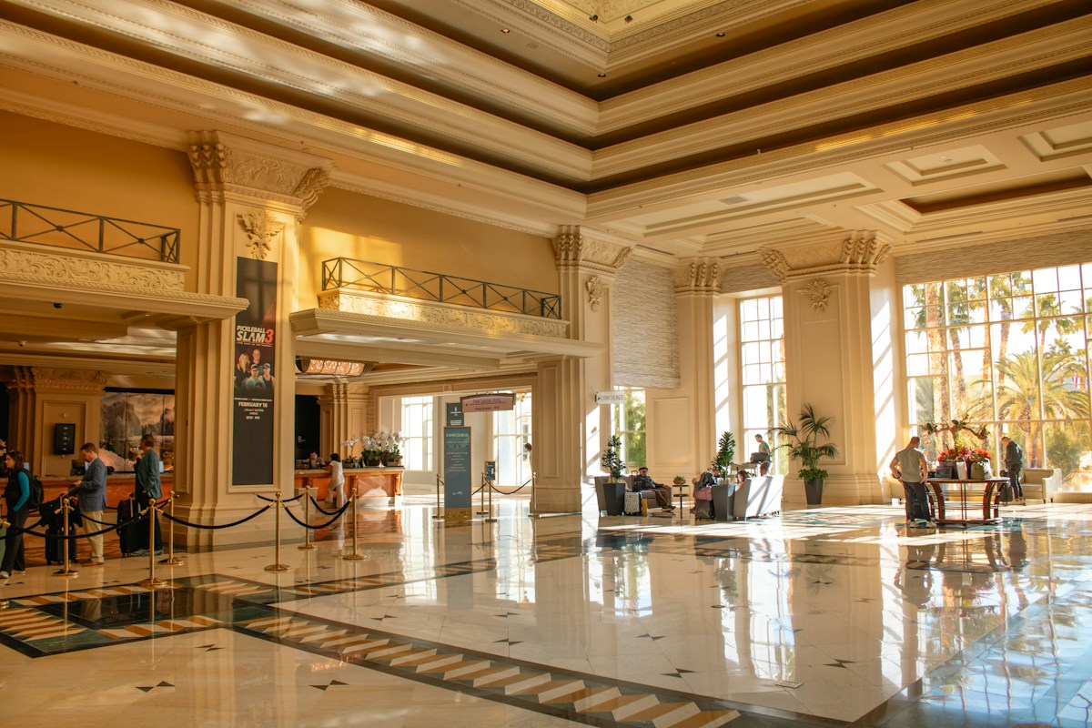 Guests with luggage crossing a sunlit grand hotel lobby, the arrival pattern that length-of-stay controls are built to shape