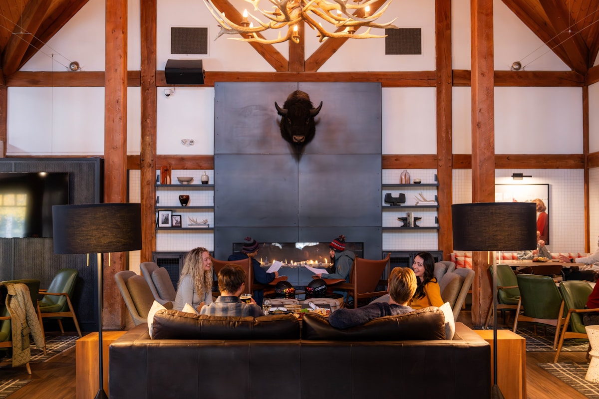 Guests gathered around the fireplace in a warm timber-framed mountain lodge lounge